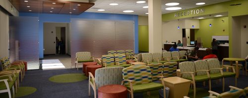 A panoramic image of the Peach Tree Health reception area with lots of comfortable chairs and very colorful walls. The reception desk is in the background to the right with the entrance to the left