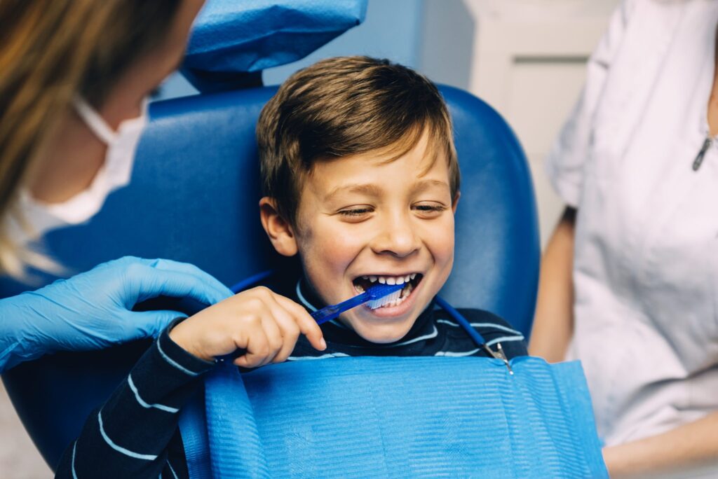 Doctor dentist teaching a child to brush teeth. - Peach Tree Health