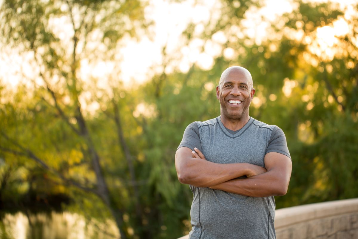 Man smiling and standing with his arms crossed in front of a tree