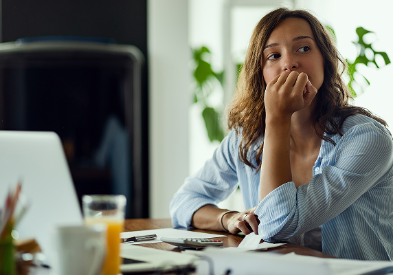 Woman sitting at a desk looking over her shoulder with a hand on her chin