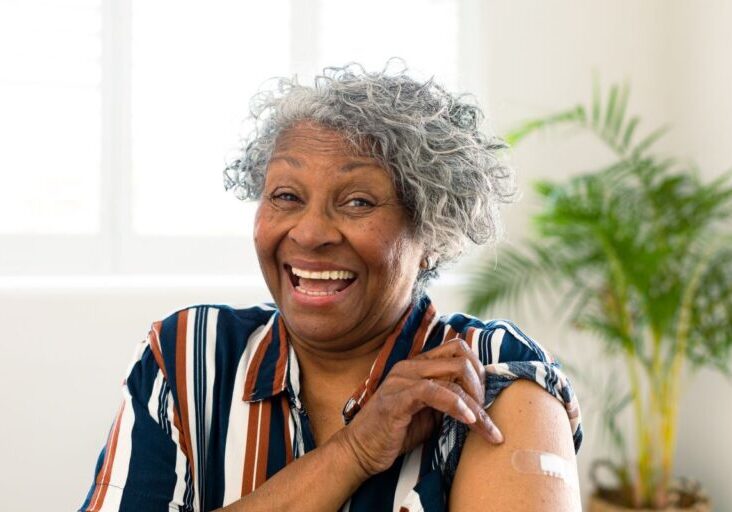 Elderly woman lifting her sleeve to show where a vaccine was received.