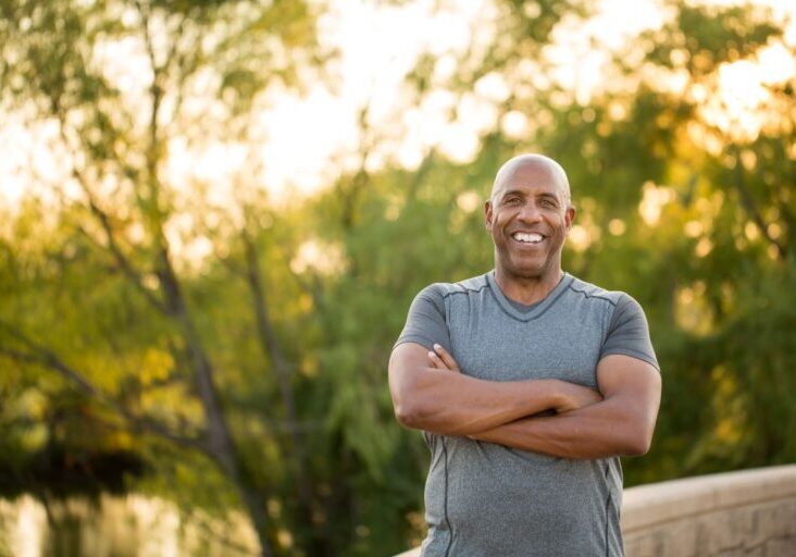Man smiling and standing with his arms crossed in front of a tree